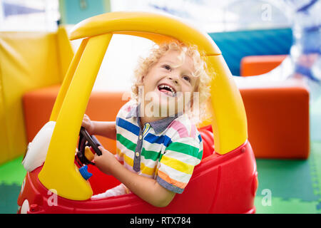 Child riding toy car. Little boy playing with big bus. Kid driving plastic truck in indoor playground or kindergarten. Toddler at day care play room.  Stock Photo