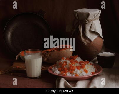 Millet porridge with pumpkin in a wooden bowl and a jug and a glass of milk Stock Photo