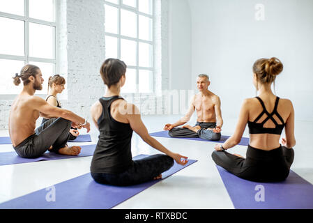 Group of young people practising yoga with experienced senior trainer in the white spacious studio Stock Photo