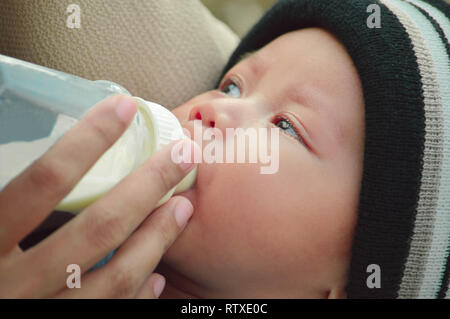 closeup portrait of beautifull baby boy drinking milk from his mother from feeding bottle Stock Photo