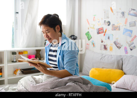 Relaxed young asian man reading book in bedroom Stock Photo