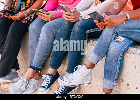 Group of modern casual woman unrecognizable sitting on the wall using modern phone devices for social networks and internet media - friendship in mode Stock Photo