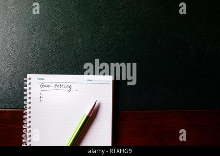 Goals setting to be written on a notebook with pen on green table Stock Photo
