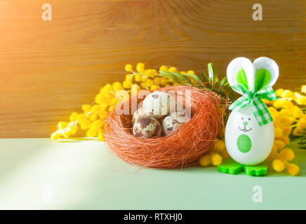 Easter background. Easter bunnies and Easter eggs in the nest near the mimosa flowers, free space for festive Easter text Stock Photo