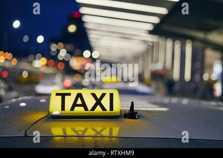 Lighting taxi sign on the roof of car against airport terminal at night. Stock Photo