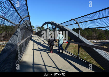 A couple crosses the Reedy Creek Trail pedestrian bridge over the 440 interstate in Raleigh North Carolina. Stock Photo