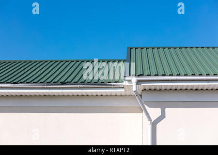 green rooftop of newly built house and white metal gutter pipes and downspout on blue sky background Stock Photo