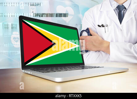 Guyana healthcare system in tech theme. Guyanese flag on computer screen. Doctor standing with stethoscope in hospital. Cryptocurrency and Blockchain  Stock Photo