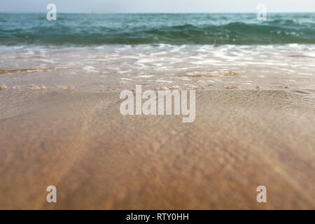 Low angle photo from ground level - beach sand wet from sea, drops of water in air, small waves and blurred ocean in distance. Abstract vacation backg Stock Photo