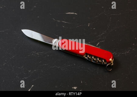 Red pocket knife on black table. Stock Photo