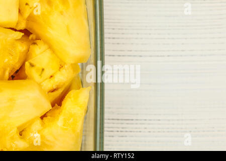 Tabletop view, detail - yellow pineapple cut in pieces, in square glass bowl, white boards desk / space for text on right. Stock Photo