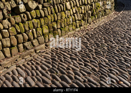 Devon, England, UK. February 2019. Cobblestone street in sunlight with a wall made from granite blocks Stock Photo