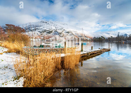 Boats and an old jetty on the snowy shores of Ullswater in the Lake District National Park in Cumbria Stock Photo