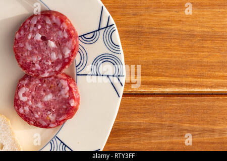 Some slices of salami on an old ceramic plate on a wooden rustic table. Food for a snack Stock Photo