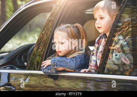 Blond caucasian children, boy and girl looking out the window while traveling with their parents in a car. Safe trip, journey driving concept. Stock Photo