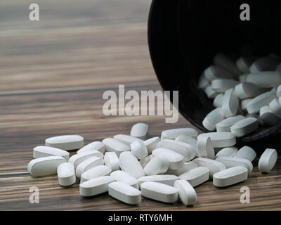White pills spilling out of a toppled dark pill bottle on wooden ground, copy space Stock Photo