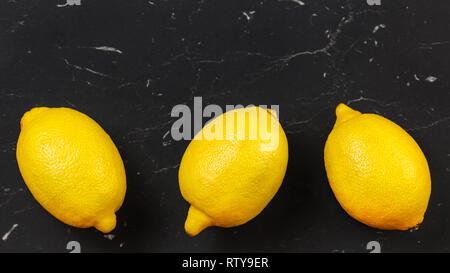 Tabletop view, three whole ripe lemons on black stone board. Space for text above Stock Photo