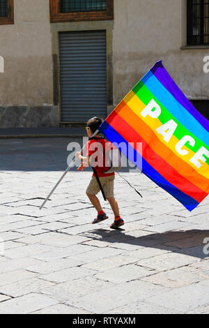 Unidentified child with rainbow flag with 'peace' (Latin and Italian: Pace) written on it, in a  bad abondoned neighbourhood. Concept of world peace a Stock Photo