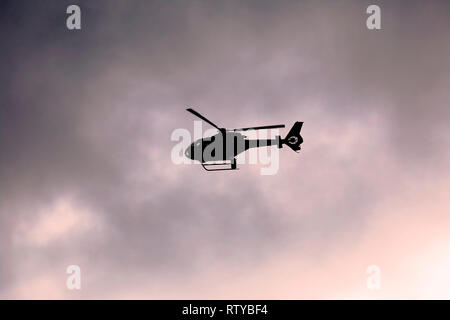 Helicopter flies in silhouette against dramatic cloudy sunset sky. Copy space. Stock Photo