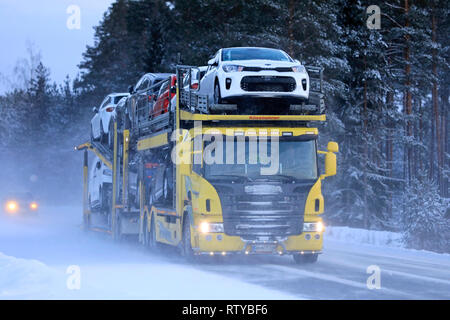 Salo, Finland - January 18, 2019: Yellow Scania car carrier truck travels in the snow trail of another vehicle on a day of winter snowfall in Finland. Stock Photo