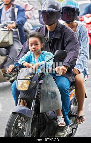 Bangkok, Thailand - June 11, 2011: A young couple driving on a motorbike, with a young girl without wearing helmet sitting in the front, caught in tra Stock Photo