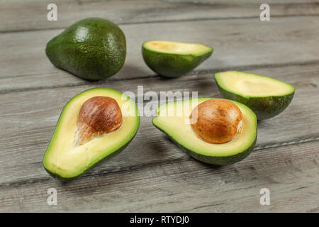 Avocados cut in half seed visible, one whole green pear in background, on gray wood desk Stock Photo