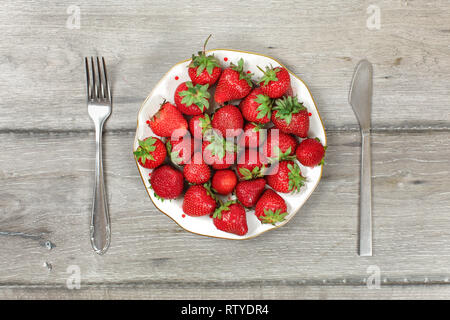 Tabletop view, plate with strawberries on gray wood boards desk, fork and knife next to it - ready to eat healthy snack concept. Stock Photo