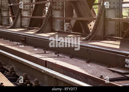 Rail bridge, detail on tracks, steel plates, large nuts and bolts lit by sun. Stock Photo