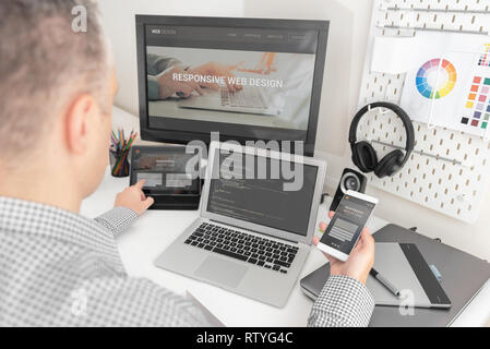 Web designer, programmer working with responsive web template. Multiple devices on desk. Stock Photo