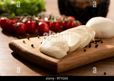 Mozzarella cheese on wooden chopping board. Cherry tomatoes in background. Wooden table with Italian food composition Stock Photo