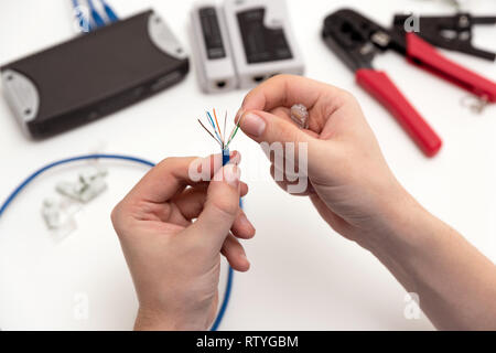 Technician holding twisted pair internet cable and RJ45 plug. Technician repairing network with cable crimper Stock Photo
