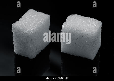 two pieces of sugar cubes on a black background - detailed macro image, photographed in studio with atrificial light Stock Photo