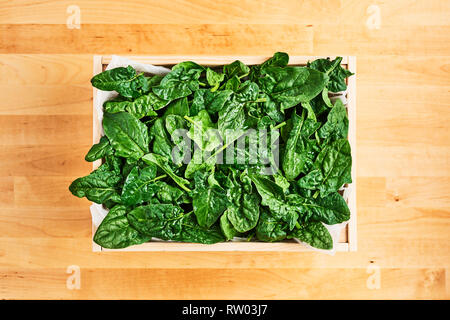 Fresh spinach leaves with water drops in wooden box on wooden table. Top view with copy space for text. Stock Photo