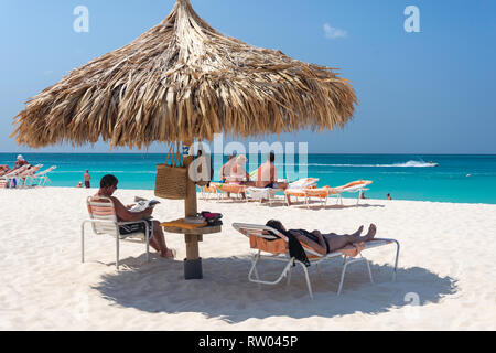 Couple relaxing under straw parasol,  Eagle Beach, Oranjestad District, Aruba, ABC Islands, Leeward Antilles, Caribbean Stock Photo