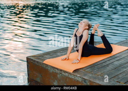 little girl doing yoga and pilates stretching up on the river bank at sunset Stock Photo