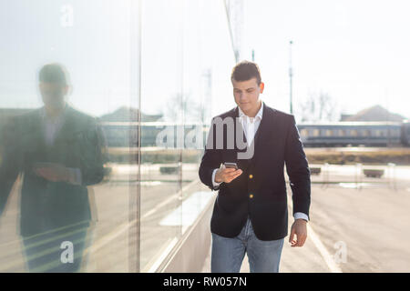 Young and Casual Businessman Using Smartphone while Walking Outside of Office Building Stock Photo