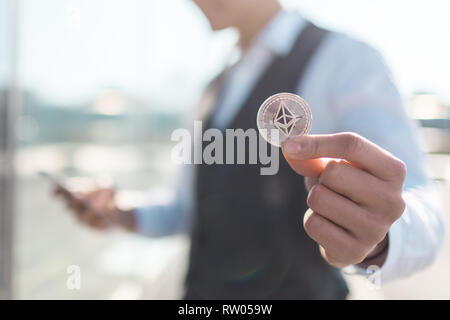 Ethereum cryptocurrency coin in a young businessman hand. Disruptive blockchain technology concept and transfer of wealth. Stock Photo