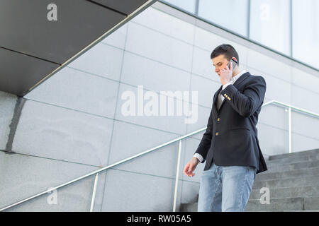 Young and Casual Businessman Using Smartphone while Walking Outside of Office Building Stock Photo