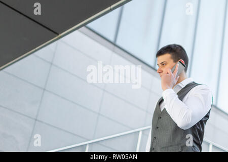 Young and Casual Businessman Using Smartphone while Walking Outside of Office Building Stock Photo