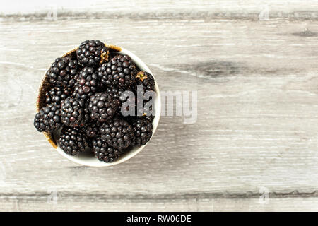Tabletop view, small ceramic cup with blackberries on gray wood desk. Space for text on the right. Stock Photo