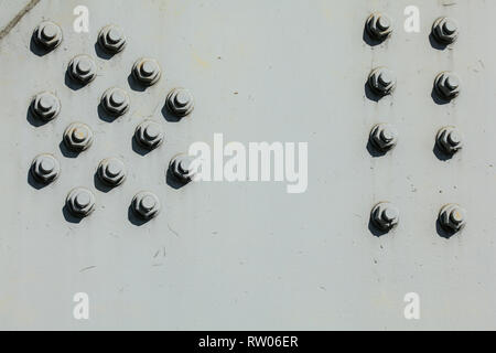 Large nuts and bolts on gray steel plate of rail bridge, lit by bright sun. Abstract industrial background. Stock Photo