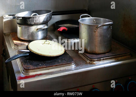 Dirty pots and pans are placed on a stainless steel electric stove on the galley on the ship Stock Photo