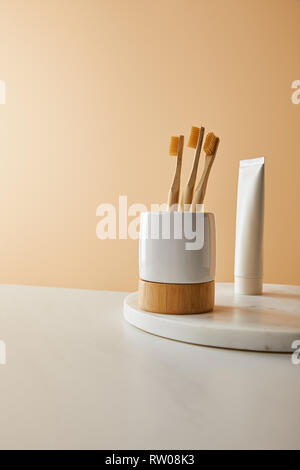 marble round board with toothpaste in tube and bamboo toothbrushes in holder on white table and beige background Stock Photo