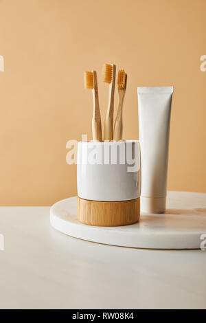 toothpaste in tube and holder with bamboo toothbrushes on white marble surface and beige background Stock Photo