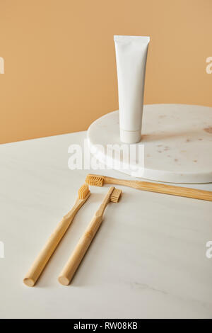 marble round board with toothpaste in tube and bamboo toothbrushes on white table and beige background Stock Photo