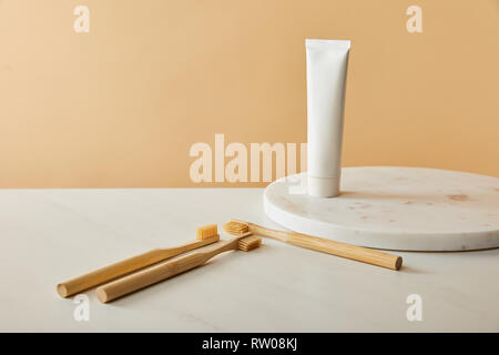 marble round board with toothpaste in tube and bamboo toothbrushes on white table and beige background Stock Photo