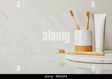 round board with toothpaste in tube, holder and bamboo toothbrushes on white marble background Stock Photo