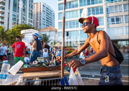 RIO DE JANEIRO - FEBRUARY 28, 2017: A Brazilian street vendor pushes a shopping cart with merchandise to sell to crowds of young people at Carnival. Stock Photo