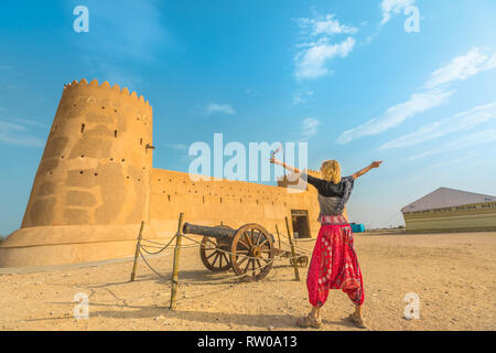 Travel in North of Qatar. Carefree woman at Al Zubara Fort, a historic Qatari military fortress, Middle East, Arabian Peninsula. Blonde tourist