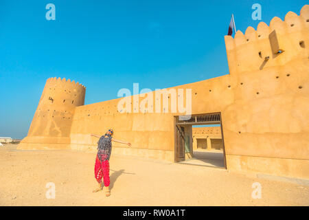 Travel in North of Qatar at Al Zubara Fort. Happy woman at entrance of old castle, a historic military fortress in Middle East, Arabian Peninsula